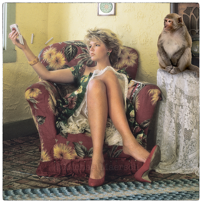 A pretty girl sitting in a chair with a monkey sitting on a small, lace-covered table beside her